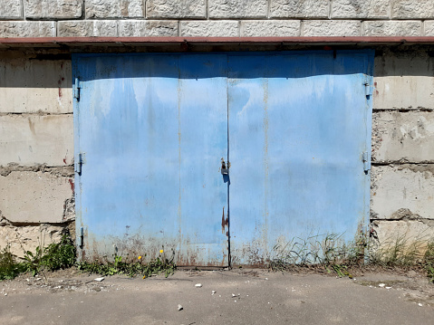Industrial Zone. A blue iron gate in a concrete block wall. Ruin. Summer.