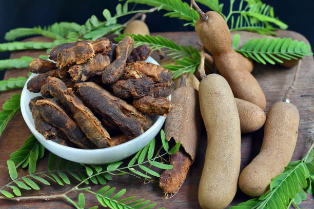 pasta di tamarindo o succo in ciotola bianca sul tavolo di legno e accanto alle foglie mature di tamarindo e tamarindo sparse con sfondo nero - tamarindo foto e immagini stock