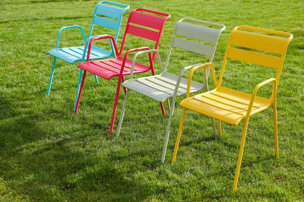 istock Four multi-colored chairs stand on a green lawn on a summer evening. Image of a comfortable place to relax in an urban environment. Sunset light, long shadows. 1319501586