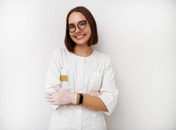 jeune stagiaire féminin de docteur de sourire posant avec les bras croisés sur le fond blanc avec l’espace de copie - esthéticienne photos et images de collection