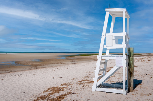 A white wooden lifeguard chair overlooks the wide expanse of sand at low tide at Chapin Beach  in Dennis, Massachusetts on a May afternoon.