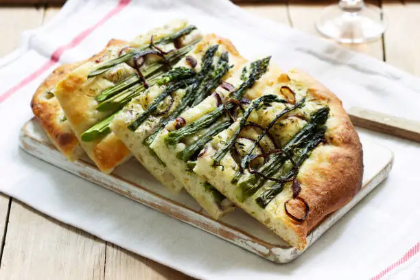 Focaccia or pizza with asparagus, onions, olives and herbs. Rustic style, selective focus.