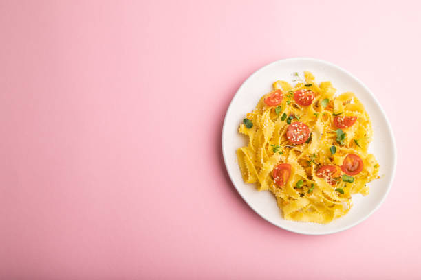 istock Reginelle semolina pasta with tomato, eggs, sesame and microgreen sprouts on a pastel pink background. Top view, flat lay, copy space. 1319508082
