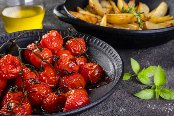 plate of confit tomatoes  and roasted potatoes with rosemary in iron casserole on dark background plate of confit tomatoes  and roasted potatoes with rosemary in iron casserole on dark background. confit stock pictures, royalty-free photos & images