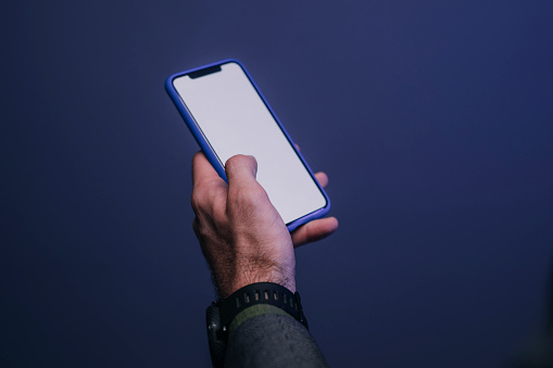 A close up shot of an anonymous man's hand holding a smartphone, dark blue background