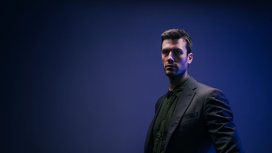 A portrait of a handsome Caucasian man wearing a suit and standing against a dark blue background