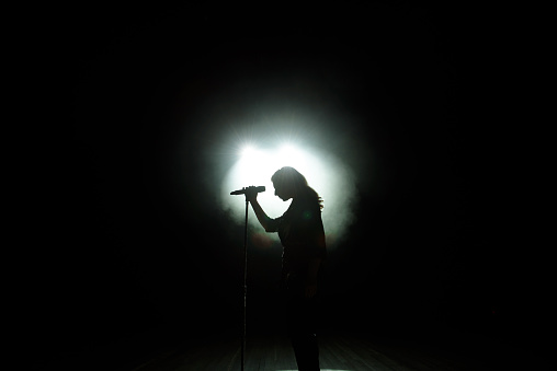 Black silhouette of female singer with white spotlights in the background.