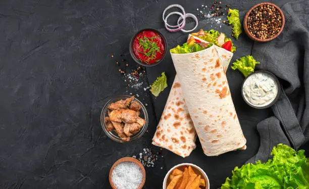 Shawarma with vegetables, salad and chicken on a black background with ingredients. Top view, copy space.