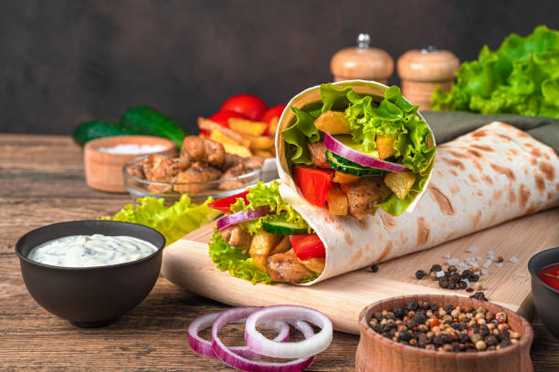 Juicy shawarma with fresh vegetables, meat and French fries on a brown wooden background Juicy shawarma with fresh vegetables, meat and French fries on a brown wooden background. Side view, copy space. shawarma stock pictures, royalty-free photos & images