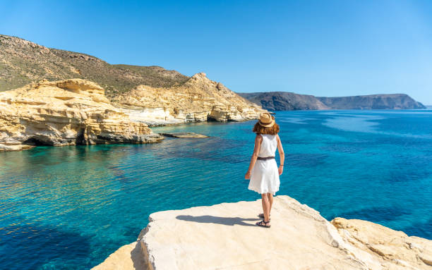 A young woman in a white dress looking at the sea in Rodalquilar in Cabo de Gata on a beautiful summer day, Almería. Mediterranean sea, spain stock photo