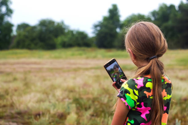 Defocus Selfie girl. Little girl takes a selfie by hand. Reflection on screen. Back view of preteen girl in summer standing on the meadow and taking a selfie on the phone. Generation z. Out of focus Defocus Selfie girl. Little girl takes a selfie by hand. Reflection on screen. Back view of preteen girl in summer standing on the meadow and taking a selfie on the phone. Generation z. Out of focus. child 10 11 years 8 9 years cheerful stock pictures, royalty-free photos & images