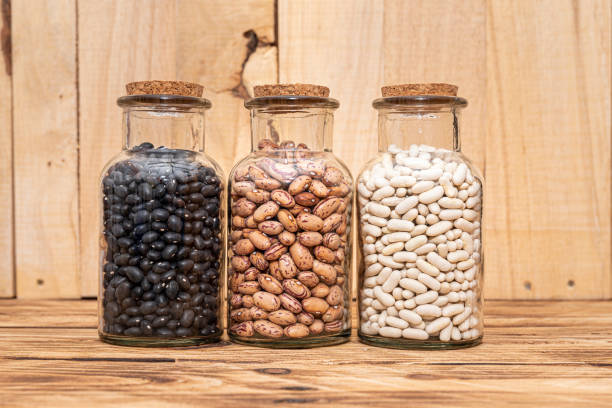 Three bottles of dried beans, Black Beans, White Beans and Borlotti Beans on a natural woode background. Healthy nutritional ingredients.