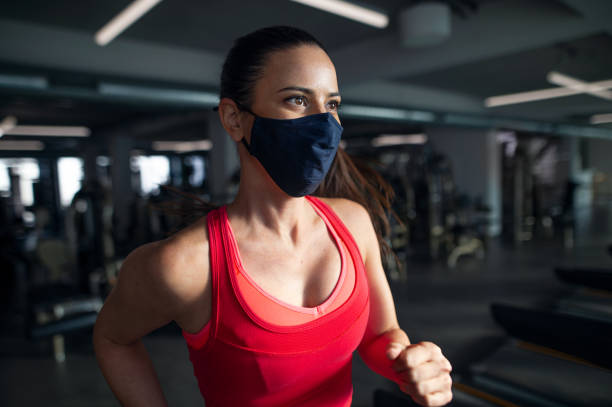 istock Woman with face mask doing exercise on treadmill in gym, coronavirus concept. 1319529421