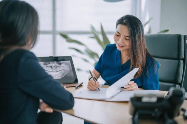 dentista chinesa asiática explicando imagem de raio-x médico para uma paciente do sexo feminino em seu consultório - equipamento dentário - fotografias e filmes do acervo