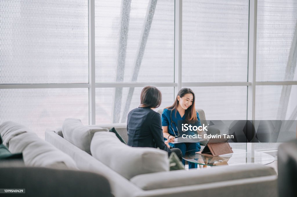 Asian chinese female doctor explaining medical report To a female Patient at her office sofa Doctor Stock Photo