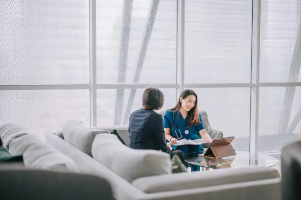 Photo of Asian chinese female doctor explaining medical report To a female Patient at her office sofa