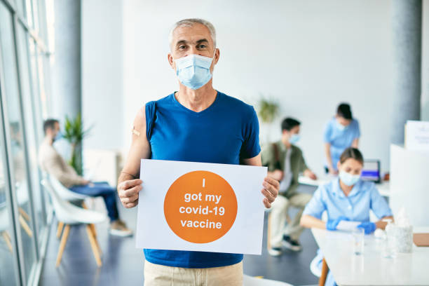 istock Happy mature man holding supportive placard during coronavirus immunization at vaccination center. 1319550966