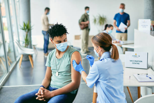 Young African American man getting vaccinated against coronavirus at vaccination center. Young black man receiving COVID-19 vaccine during immunization at vaccination center. covid 19 vaccine stock pictures, royalty-free photos & images