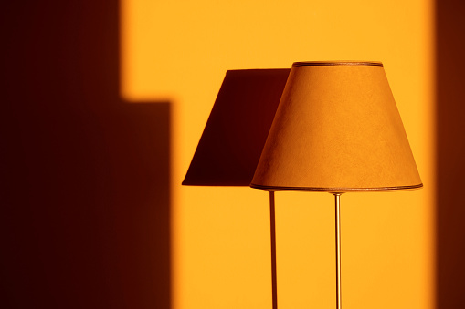 Yellow lamp shade with metal stand illuminated by sunset light with a harsh shadow on the wall