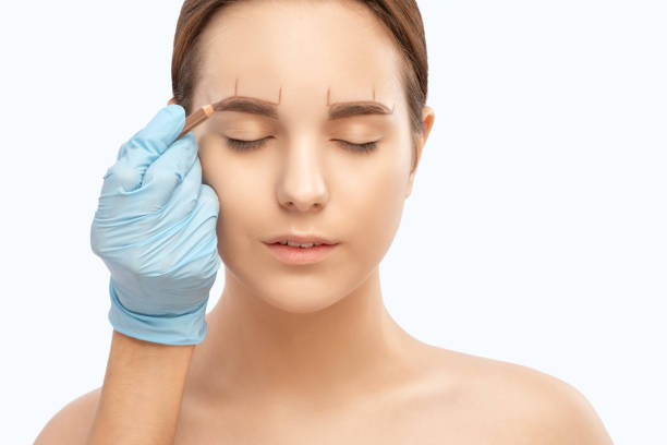 istock Make-up artist makes markings with white pencil for eyebrow and paints eyebrows. Professional makeup and facial care. 1319557682