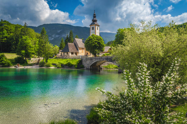 Traditional alpine church on the shore of the lake Bohinj Flowery lake shore and old stone bridge over the lake Bohinj. Traditional old church on the shore of the lake Bohinj, Slovenia, Europe slovenia stock pictures, royalty-free photos & images