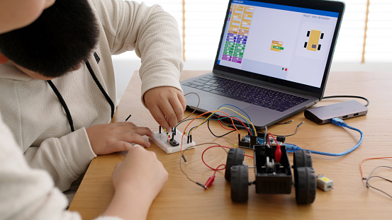 Young asia student remotely learn online at home with parent in coding robot car and electronic board cable in STEM, STEAM, mathematics engineer science technology computer code in robotics for kids.