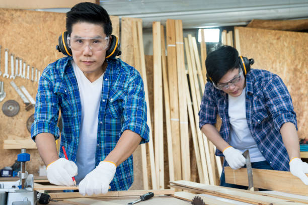 istock Carpenters working in teamwork. Two young man as carpenter apprentices work on the circular saw in the workshop. 1319565529