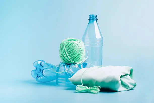 Photo of The concept recycling plastic. Empty plastic bottle and recycled polyester fiber, synthetic fabric blue background
