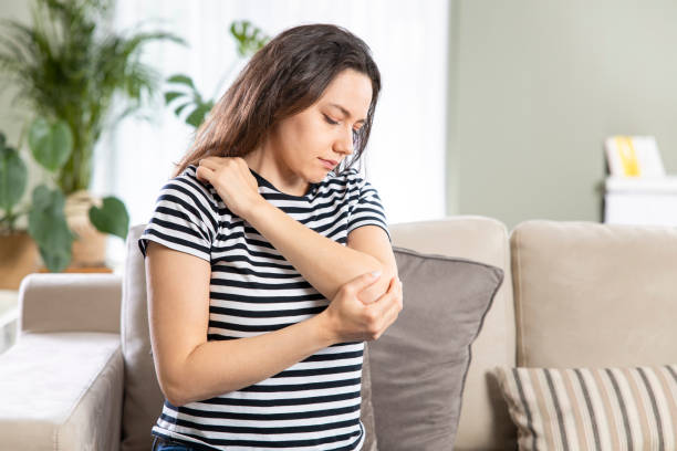 Young woman suffering from pain in elbow at home Young woman is sitting at home on her sofa and touching the her elbow while suffering from elbow pain human joint stock pictures, royalty-free photos & images