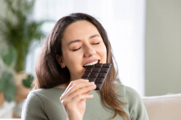 Woman biting a chocolate bar Cheerful young woman eating chocolate at home dark chocolate stock pictures, royalty-free photos & images