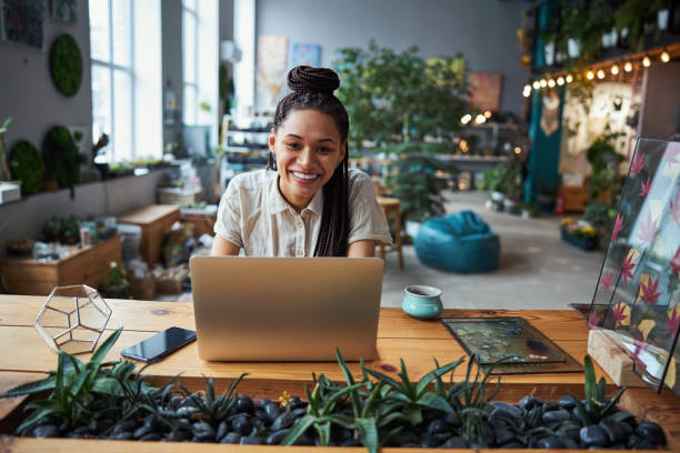 istock Joyous florist with cornrows sitting at a laptop in the workshop 1319577371