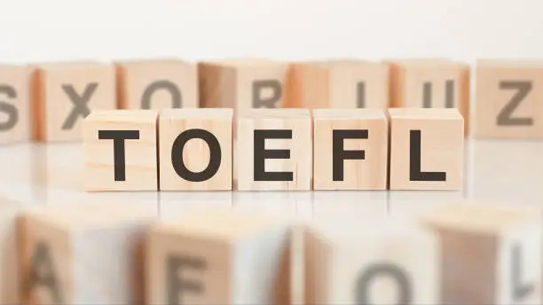 Toy wood blocks with letters toefl on a table with light background, selective focus. TOEFL - short for test of english as a foreign language
