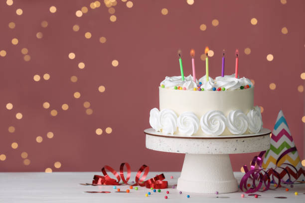 istock Birthday cake with burning candles and decor on white table against blurred festive lights, space for text 1319578113