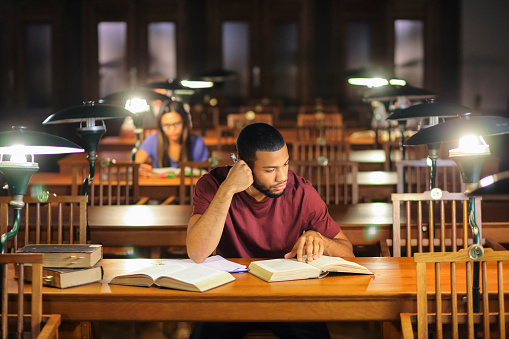 People reading books in the library. Afro-american man and asian woman sitting in the library reading room and studying for exam late at nigh.