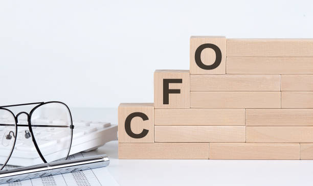 Three wooden cubes with letters CFO on the white table with keyboard and glasses stock photo