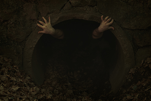Small dark tunnel opening with two hands with twisted fingers poking out and holding to edge, someone trying to get out