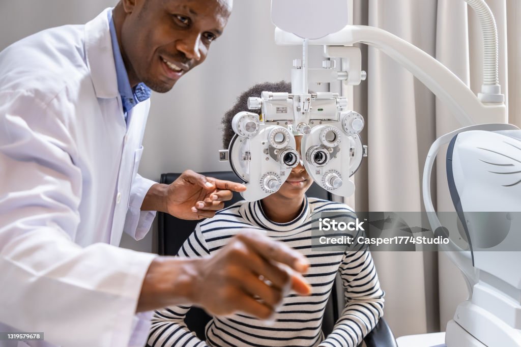 African young woman girl doing eye test checking examination with male man optometrist using phoropter in clinic or optical shop. Eyecare concept. Ophthalmologist Stock Photo