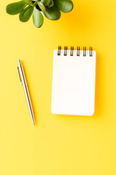 istock Office desktop with empty notebook and pen on yellow background. Business concept. Top view 1319582799