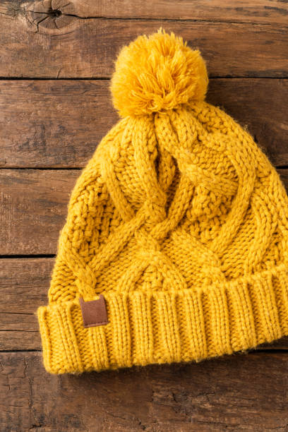 istock Yellow winter hat with pompon on wooden background. Top view 1319582926