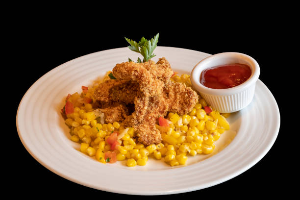 Breaded chicken wings with boiled corn and ketchup. Food on a white plate isolated on a black background Breaded chicken wings with boiled corn and ketchup. Food on a white plate isolated on a black background. sticky sesame chicken sauces stock pictures, royalty-free photos & images