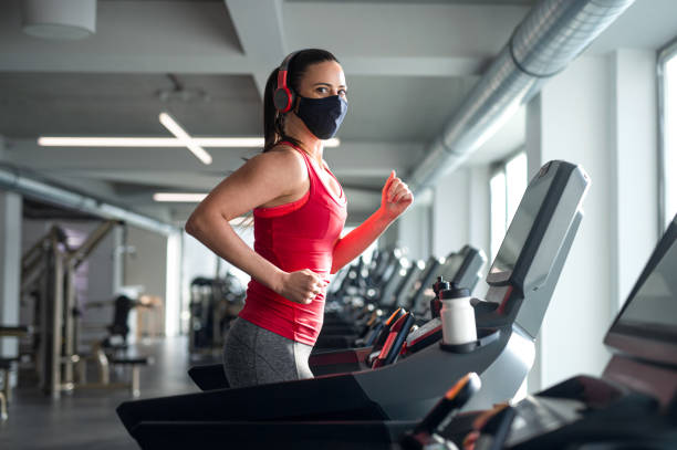 istock Woman with face mask doing exercise on treadmill in gym, coronavirus concept. 1319585452