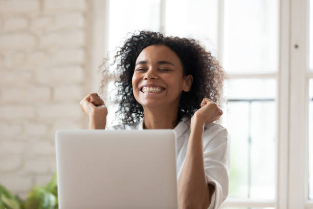 Overjoyed smiling young african ethnicity employee celebrating online success. Overjoyed smiling young african ethnicity female employee feeling excited of reading email on computer with amazing news, celebrating success or achievement, job promotion, career opportunity concept. virtual event photos stock pictures, royalty-free photos & images