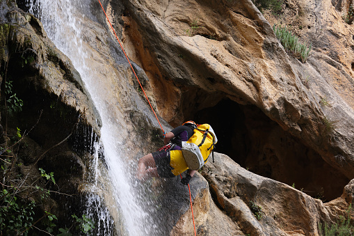 Young Lady with safety equipment abseiling through a waterfall sometimes referred to as Canyoneering