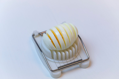 Sliced white chicken egg on slicer on white background.
