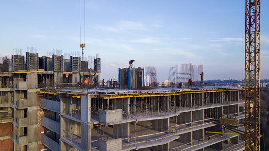 A worker on a high-rise building hammers in a formwork for pouring concrete against the backdrop of a sunset sky, in the evening.
