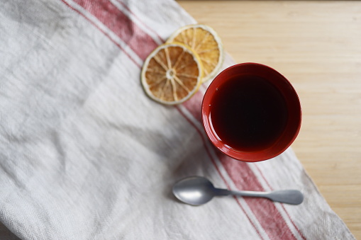 Istanbul, Turkey-May 12, 2021: Black tea in ceramic red cup on wooden bamboo tray. Linen beige napkin, spoon and dried orange slices around teacup. The napkin has a red stripe on the edge. Shot with Canon EOS R5.