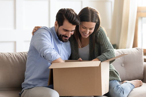 Excited millennial Caucasian couple unpack unbox package shopping online on internet from home together. Happy young man and woman open parcel with web order. Good delivery service concept.