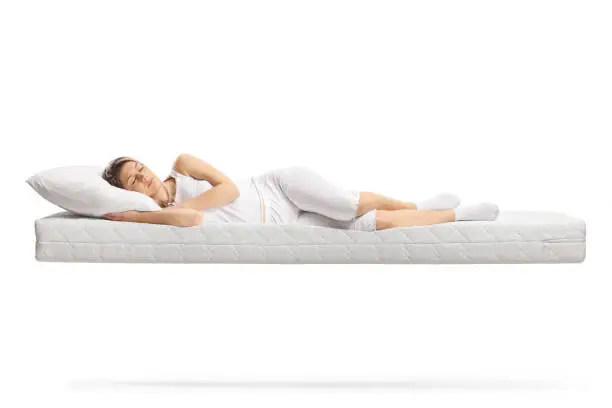 Young woman in white pajamas sleeping on a floating mattress isolated on white background