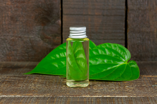 Betel Essential oil in bottle and green leaf on wooden table. Betel is a vine that has the heart shaped leaves.