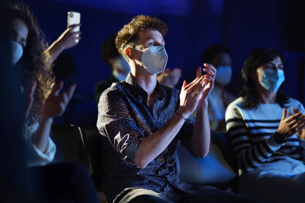 Group of people clapping while listening to presentation at conference, coronavirus concept. A group of people clapping while listening to presentation at conference, coronavirus concept. ritual mask stock pictures, royalty-free photos & images